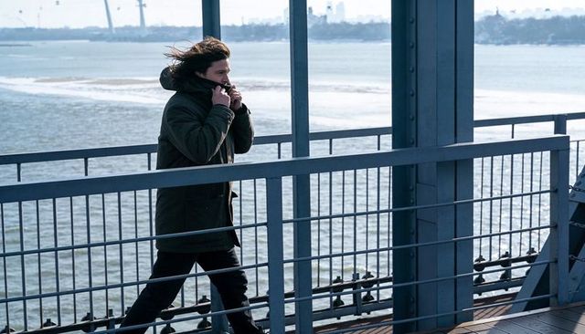 Man walking along waterfront bridge wearing heavy parka on windy overcast day