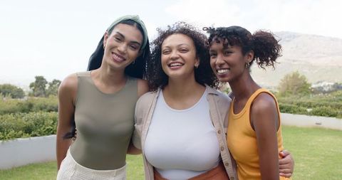 Smiling african american women friends linking arms in sunlit garden for lifestyle