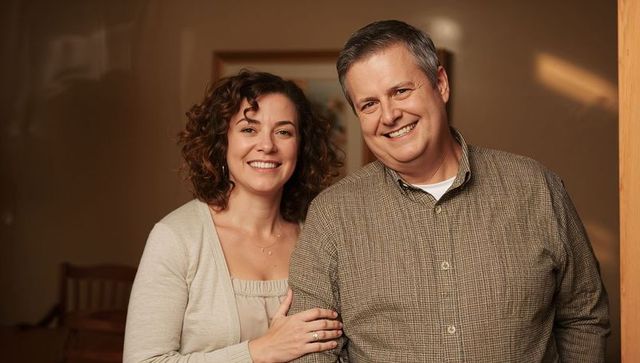 Smiling middle-aged couple in warm home portrait showing wedding ring and cozy affection