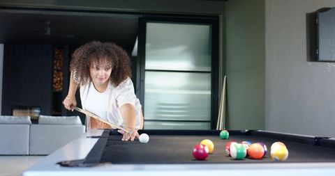Young woman lining up precision pool shot on black felt table in modern home lounge