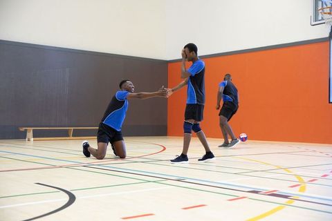 African american volleyball teammates reaching for handshake after play on indoor court