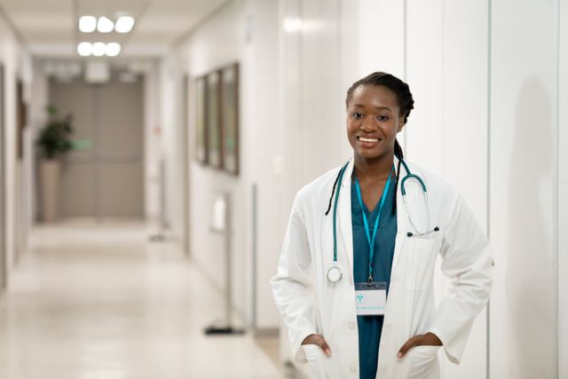 Portrait of smiling african american female doctor standing in hospital corridor, with copy space. Medical services, hospital and healthcare concept.