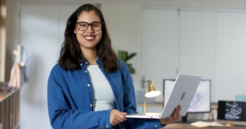 Smiling young professional holding laptop in bright modern coworking office
