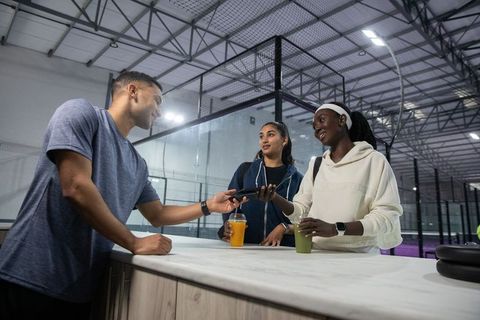 Multicultural friends exchanging smartphone at sports center counter holding smoothies