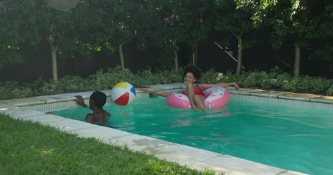 Mother and son playfully relaxing in backyard pool with float and beach ball