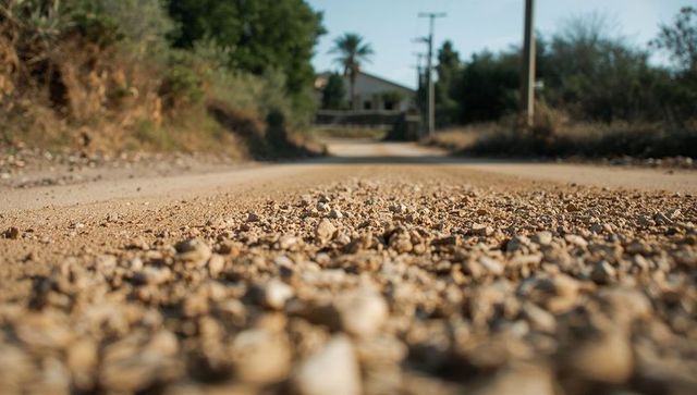 Low-angle gravel road revealing surface texture and loose pebbles in sunlit rural lane