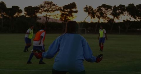 Goalkeeper guarding goal at sunset during youth soccer training session with players dribbling