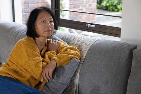 Senior Asian Woman Relaxing on Sofa Near Bright Window