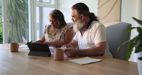 Senior couple reviewing documents at home engaging with tablet