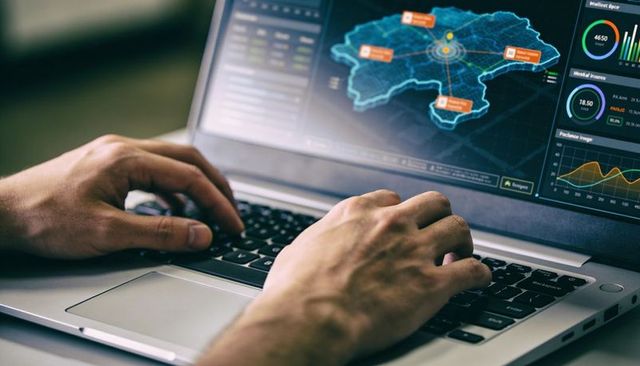 Data analyst typing on laptop with geospatial dashboard, real-time analytics display