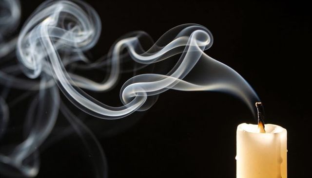 Extinguished candle emitting elegant curling smoke trails on black background