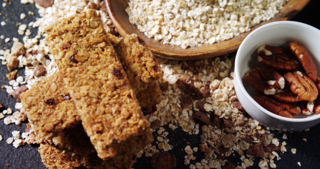 Oatmeal bars are placed alongside a bowl of raw oats and pecans, suggesting ingredients for a healthy snack. The focus on the texture and natural colors emphasizes the wholesome, nutritious aspect of the food.