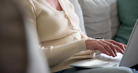 Senior Woman Typing on Laptop Relaxing on Comfortable Sofa