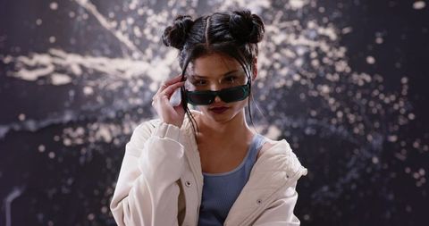Chic fashion portrait woman adjusting sunglasses wearing cream jacket with splash backdrop