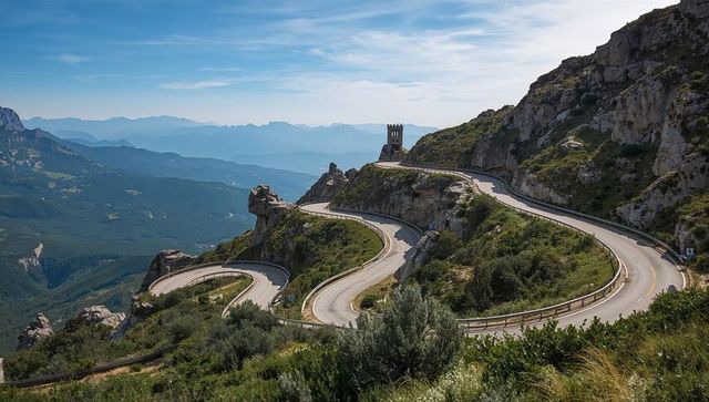 Winding Mountain Road through Alpine Pass near Ancient Stone Tower