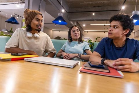 Multicultural young adults collaborating around laptop in modern coworking workspace