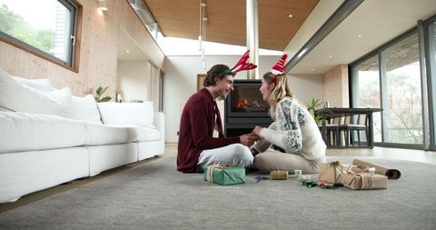 Cheerful couple wrapping christmas gifts in cozy living room