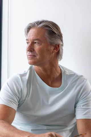 Mature man gazing out window in minimalist bright interior, contemplative portrait
