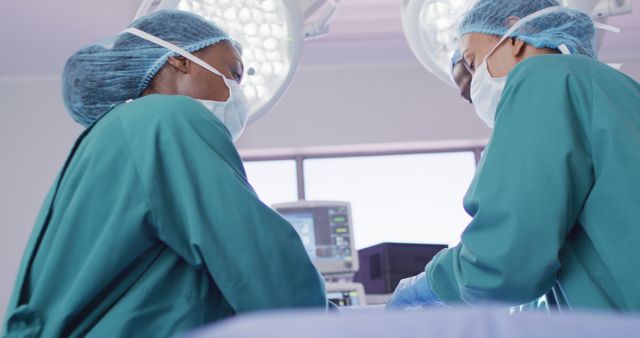 Two surgeons wearing green scrubs and surgical masks are collaborating to perform a procedure in a modern operating room. This image is ideal for healthcare publications, medical websites, and educational materials highlighting teamwork in medical settings.