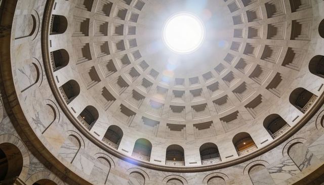 Sunlit coffered dome with central oculus over marble rotunda and ornate balustrades