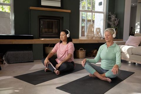 Mature women practicing guided meditation at home with headphones on yoga mats