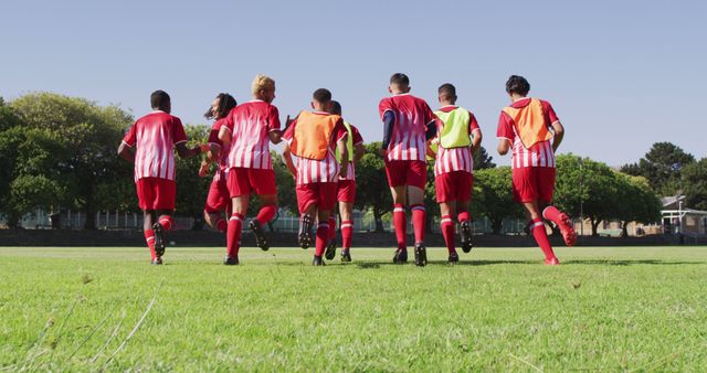 Youth soccer team running together on grassy field wearing red uniforms. Ideal for depicting teamwork, outdoor sports training, youth athletic programs, and community sports activities.