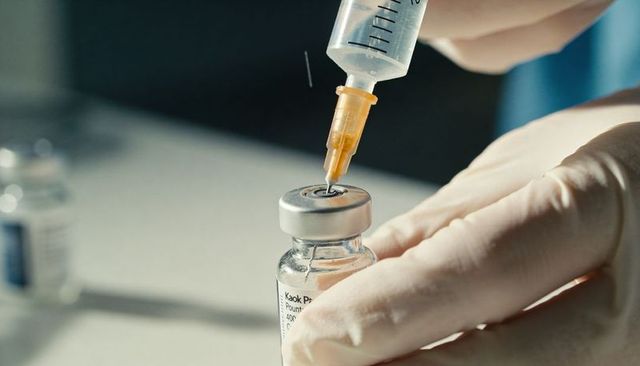 Gloved hands drawing vaccine into syringe from labeled vial closeup clinical preparation
