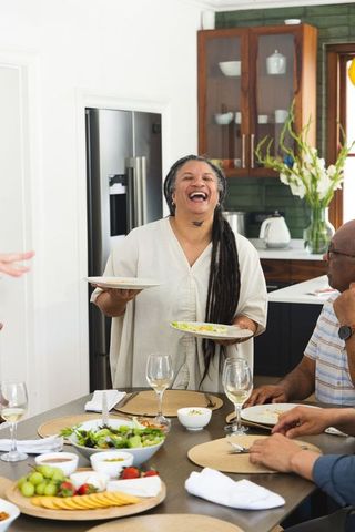 Mature woman serving plates and laughing with friends at cozy home dinner gathering