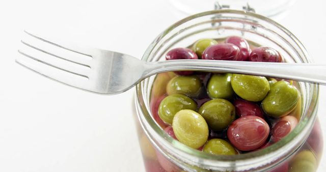 A fork rests on an open jar filled with colorful olives, with copy space. The image conveys a sense of preparing to enjoy a Mediterranean snack or appetizer.