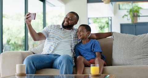 African american father and son taking selfie on sofa sharing joyful morning together
