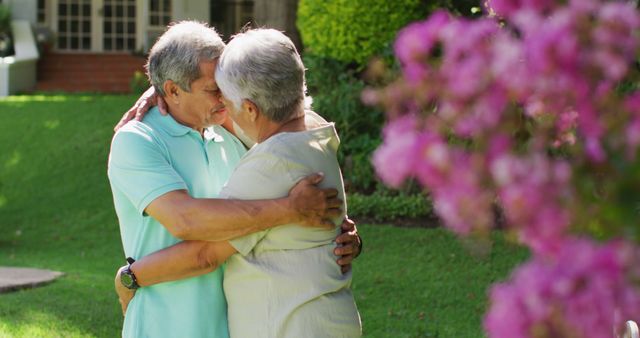 Elderly couple sharing a loving embrace in lush garden. Perfect for illustrating themes of love, companionship, and happiness among seniors. Ideal for retirement and healthcare advertisements, editorial uses, and family lifestyle content.