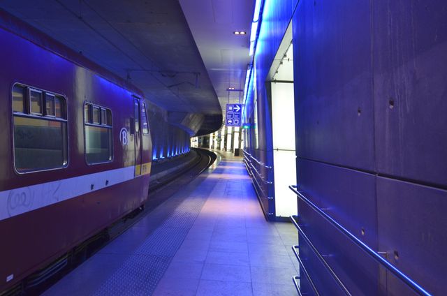 The scene depicts a modern underground train station with futuristic blue lighting. The platform is empty, enhancing the contemporary and sleek design. This visual can be used in contexts related to urban transportation, city travel, architectural designs, and future transportation solutions.