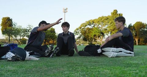 Teen cricket teammates resting and talking on grass after training during golden hour