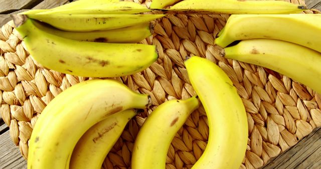 Overhead view of bright yellow bananas placed on a woven natural fiber placemat. Ideal for use in contexts related to healthy eating, organic and vegan food promotions, fresh produce advertising, tropical fruit displays, and food blogs highlighting nutritious snacks.
