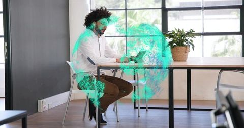 Man working on laptop with holographic green globe overlay in bright coworking workspace