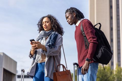 Multicultural travelers checking smartphone while standing with luggage at transit hub
