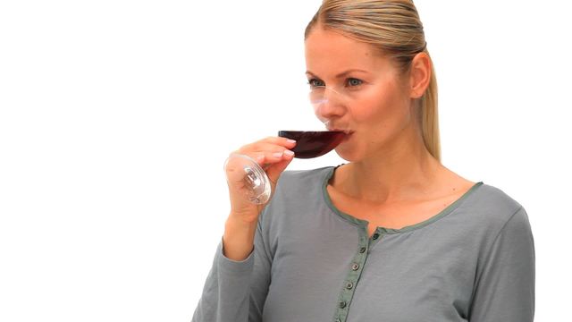 Casual blonde woman sipping a glass of red wine against a clean, white backdrop. This versatile stock image is perfect for use in articles or blogs about lifestyle, leisure, and relaxation. It can also work well in promotions or advertisements for wine brands, tastings, or events.