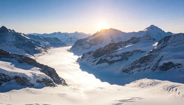 Low sun over alpine glacier valley carving vast snowfield and jagged peaks in alpenglow