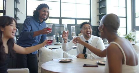Friends raising glasses and celebrating around round wooden table in modern kitchen