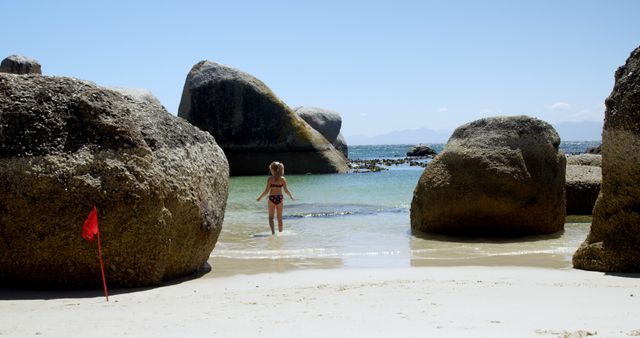 Child in swimsuit on rocky beach with sea view and red flag - Download Free Stock Images Pikwizard.com