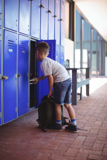 Boy taking books from locker in school corridor. Ideal for educational materials, back-to-school promotions, and articles about student life. Shows preparation and organization in a school setting.