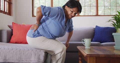 Senior woman experiencing back pain while standing from sofa
