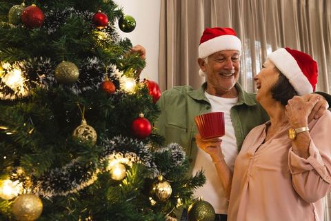 Elderly Couple Joyously Decorating Christmas Tree with Santa Hats