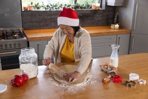 Senior Woman Wearing Santa Hat Baking Christmas Cookies in Kitchen