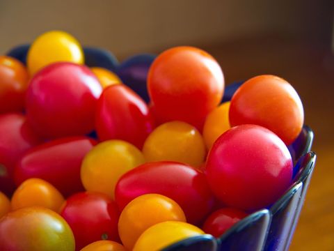 Displaying colorful cherry and grape tomatoes in blue bowl close-up, vibrant fresh produce