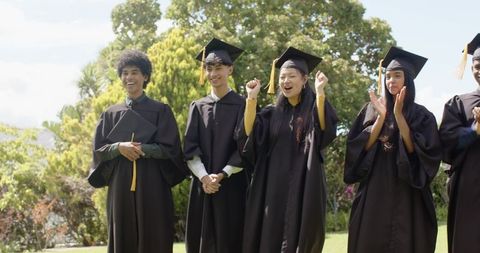 Multicultural Graduates Celebrating on Campus Lawn in Caps and Gowns During Commencement