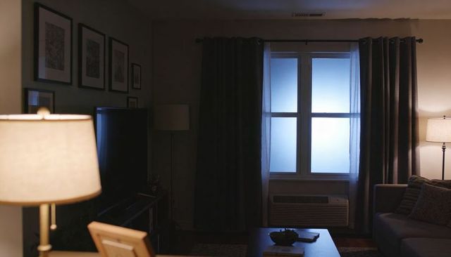 Dim living room bathing in cool blue window light with dark curtains, sofa and lamps