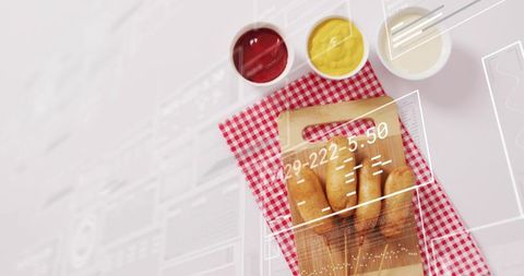 Top-down flatlay displaying wooden board with bread rolls, condiments and digital overlay