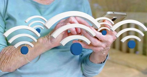 Senior woman holding smartphone tapping wi-fi icons at home connecting to internet