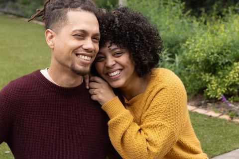 African american couple laughing and showing ring while cuddling on garden lawn